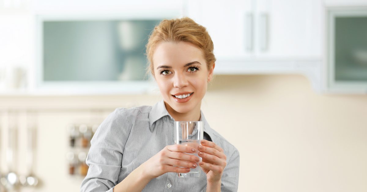 Žena v kuchyni drží sklenici vody, pitný režim při hubnutí